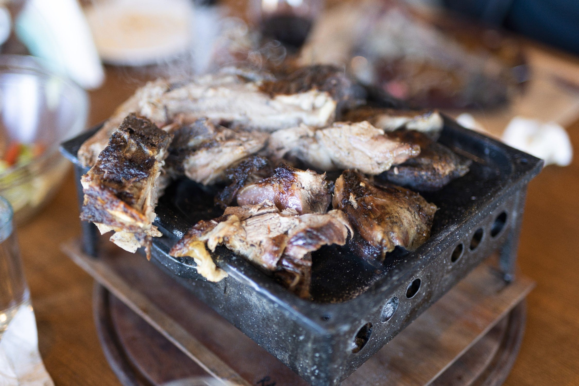 Smoky charred brown grilled meat piled on a black cast-iron tabletop grill, rustic lodge style