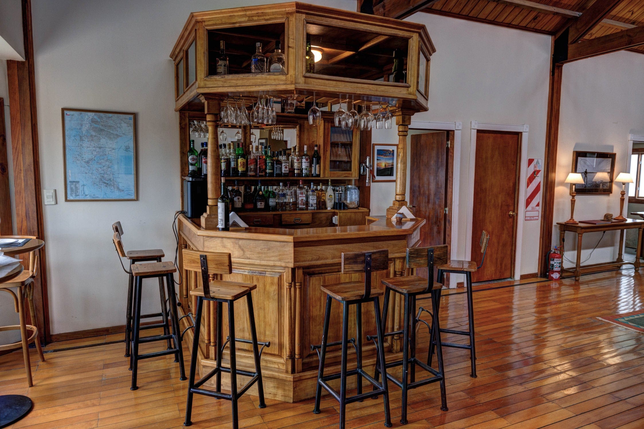 Honey-toned wooden bar with hanging wine glasses and rustic high stools in Maria Behety Lodge lounge