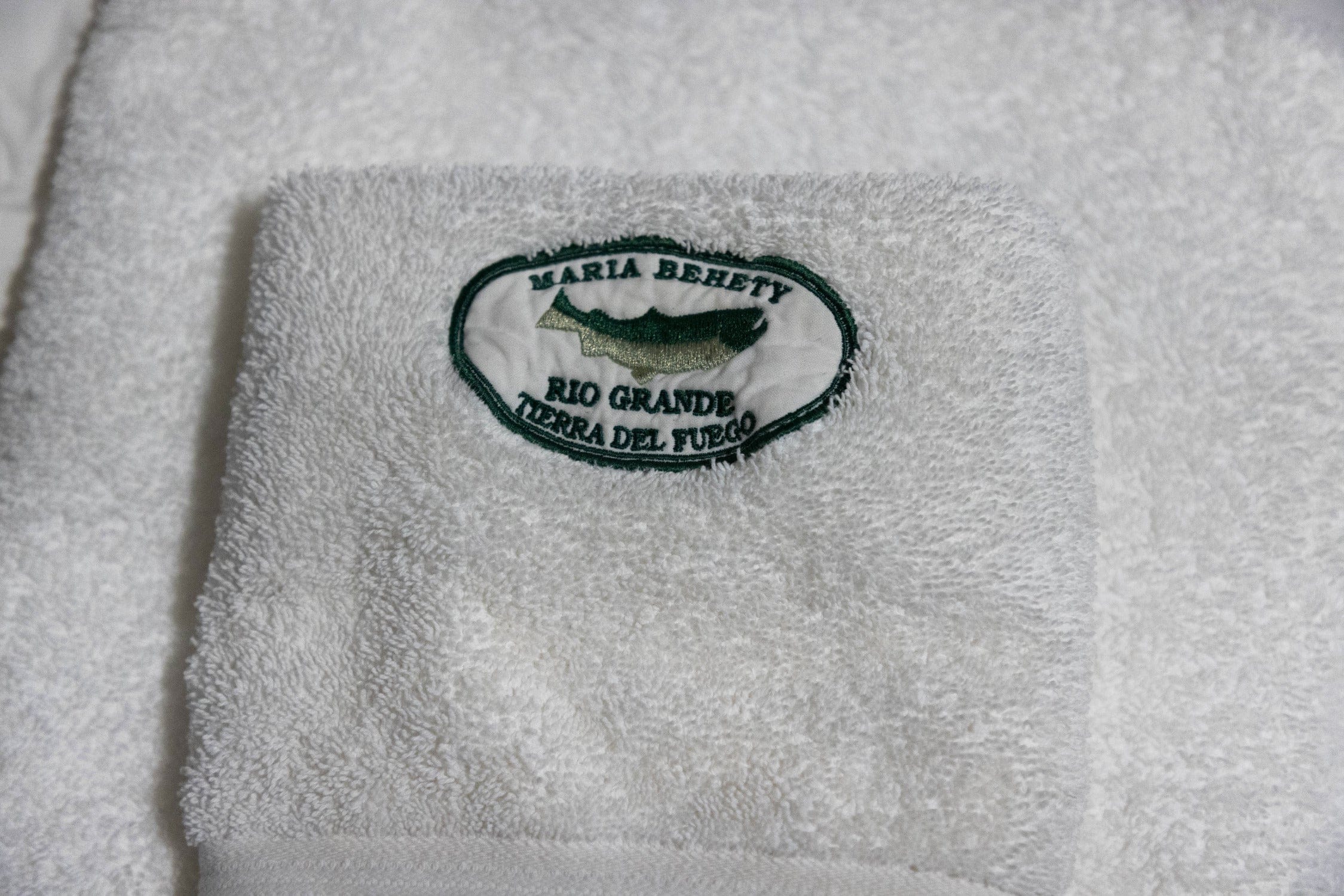 White terry cloth towel with green embroidered oval logo reading Maria Behety Rio Grande Tierra del Fuego