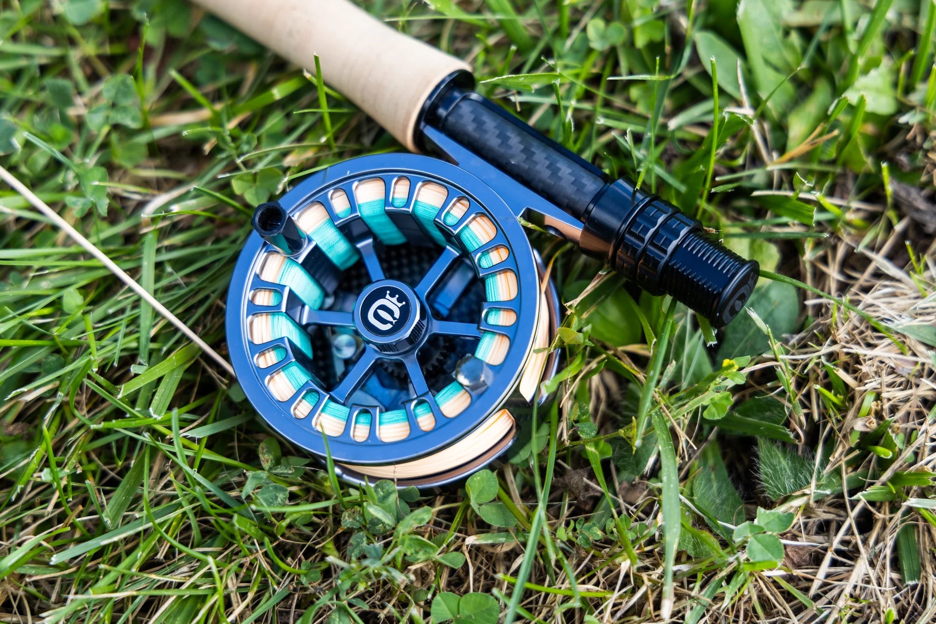 Cortland Retro Click blue anodized fly reel with turquoise and peach backing, carbon-fiber seat and cork handle on grass
