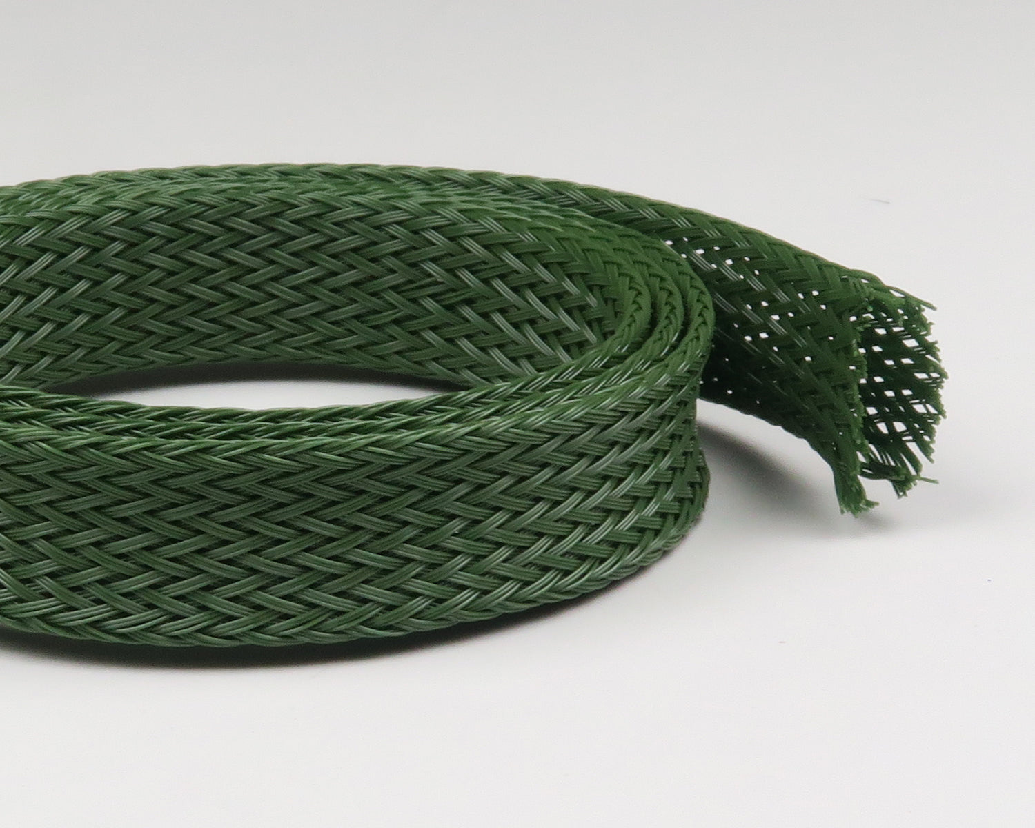 Coiled olive green braided synthetic body tubing with tight woven mesh and frayed end, flexible hollow sleeve for fly tying
