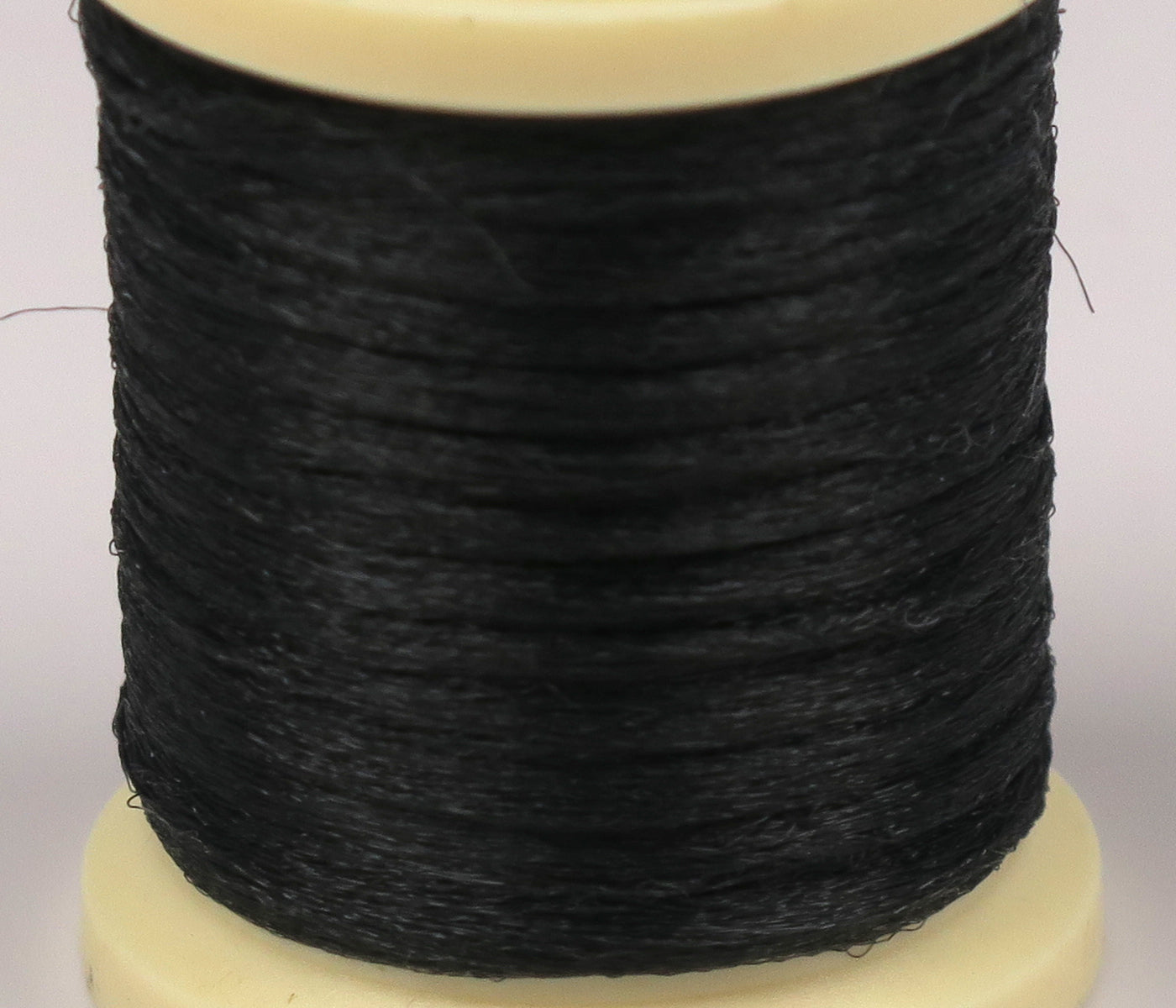 Black Hareline Antron yarn spool with fine synthetic fibers wrapped tightly on a cream plastic base, fly tying material