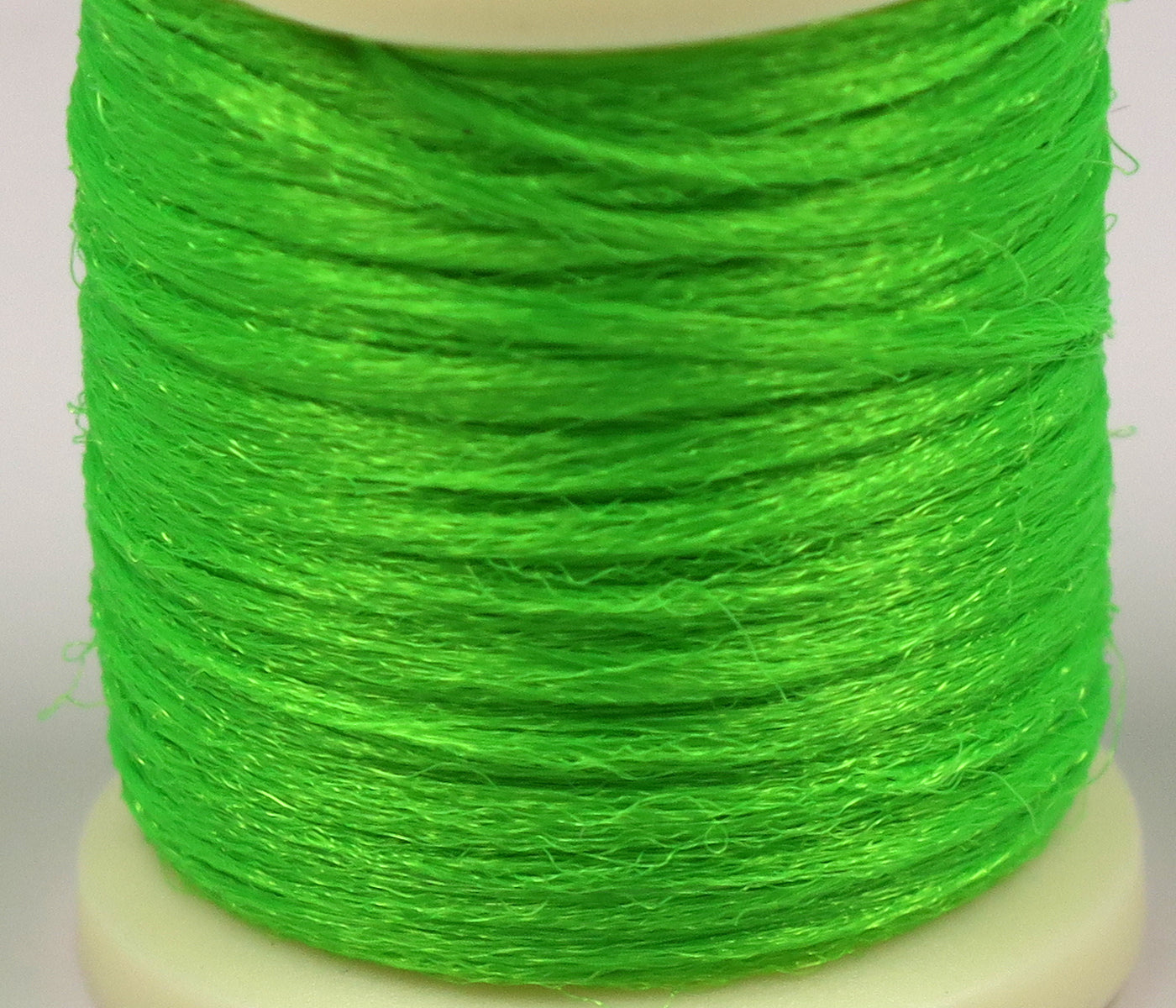 Close-up bright neon green Hareline Antron yarn spool with shiny synthetic fibers for fly tying