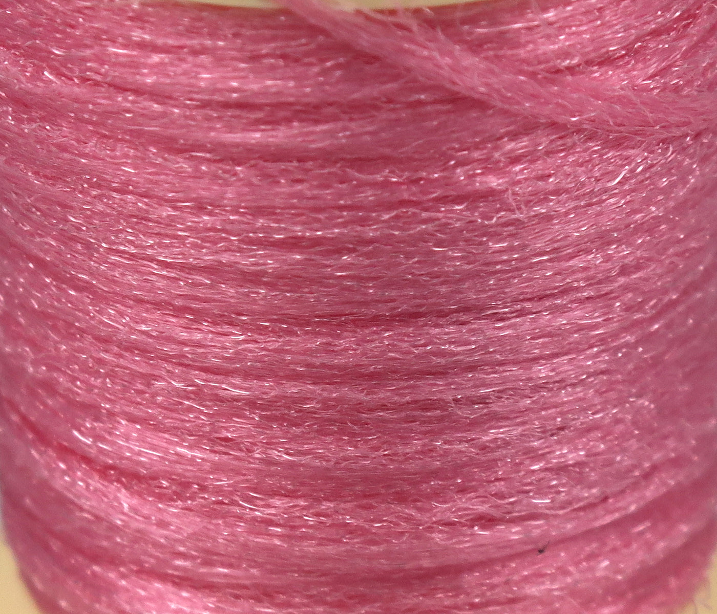 Close-up of Hareline Antron pink synthetic yarn spool with fine shimmering fibers for fly tying