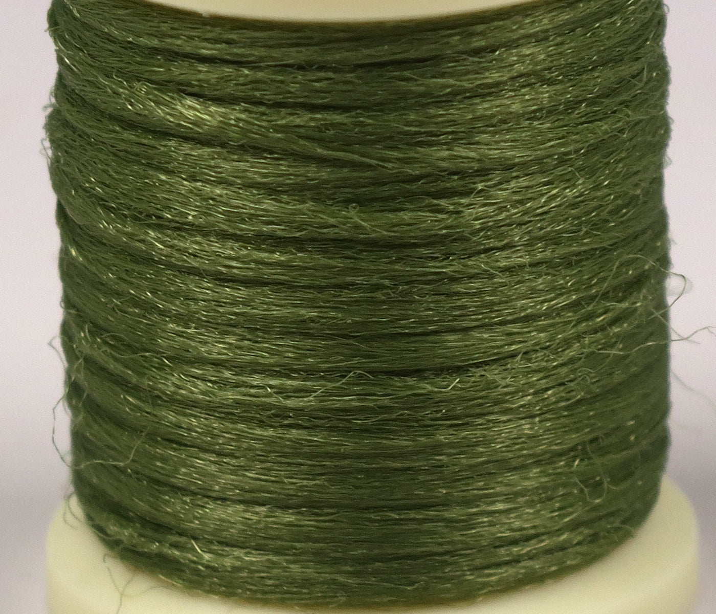 Hareline Antron yarn spool in olive green, shiny synthetic fibers for fly tying, fine textured filament wound on spool