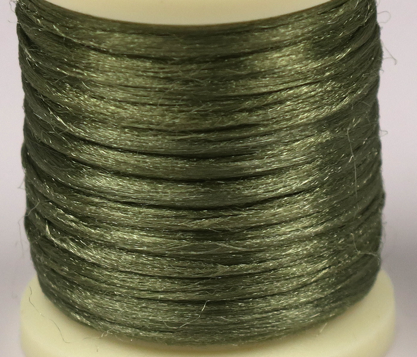 Close-up spool of Hareline Antron yarn in olive green, shiny synthetic fibers wrapped on a white plastic fly-tying spool