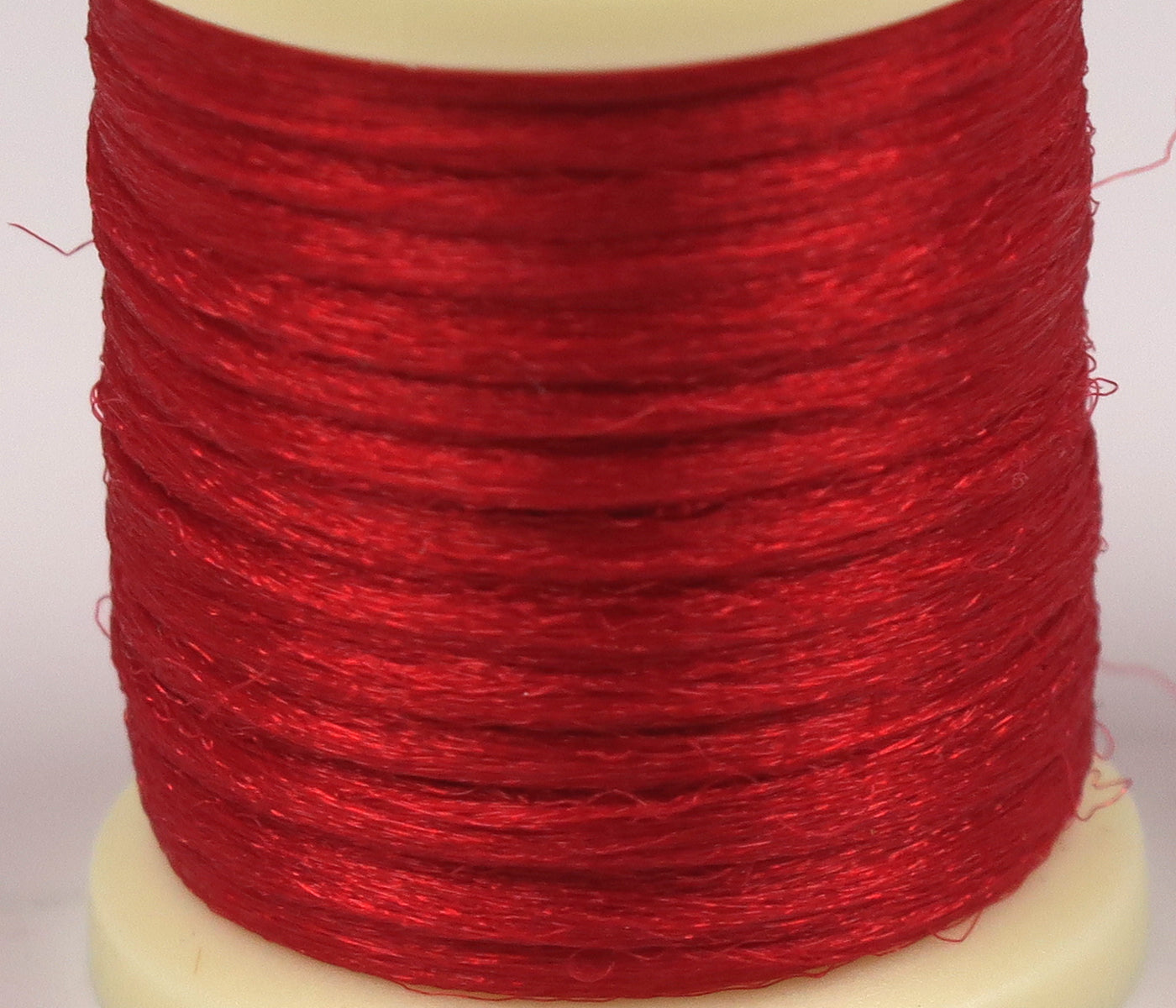Bright red shiny Antron yarn spool with fine synthetic strands for fly tying, tightly wound on cream plastic core