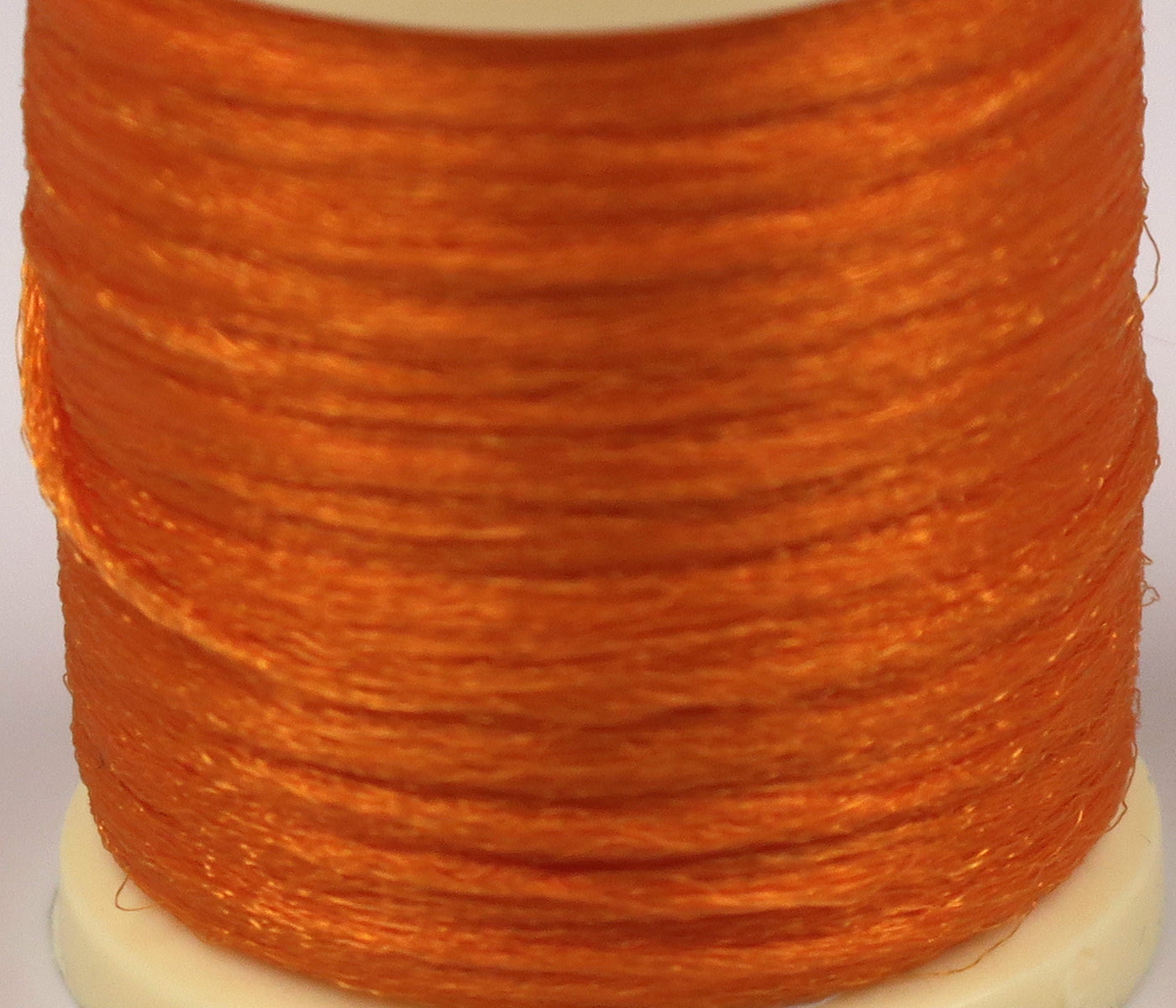 Bright orange Hareline Antron yarn with glossy synthetic fibers wound on a white spool for fly tying.