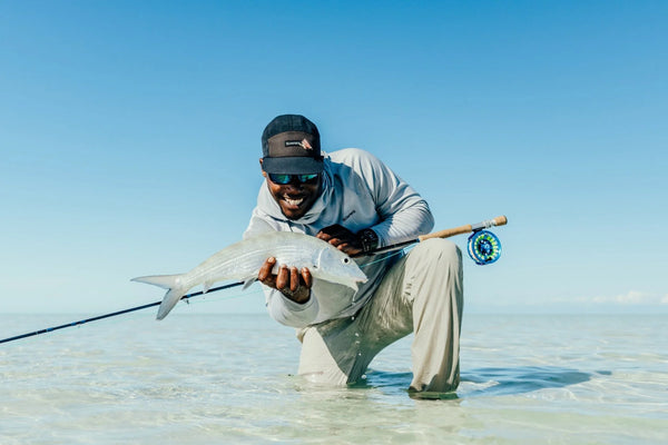 Smiling angler in gray hoodie and navy cap holding silver fish on a clear blue saltwater fly fishing trip