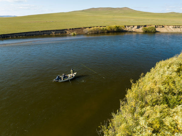 Fisherman in small boat on river with green hillside landscape and natural vegetation along grassy banks