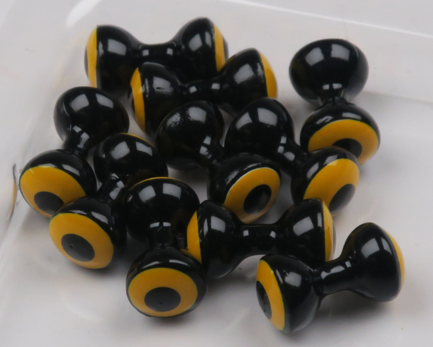 Glossy black double-pupil brass eyes with yellow ring and black center, dumbbell shape for fly tying