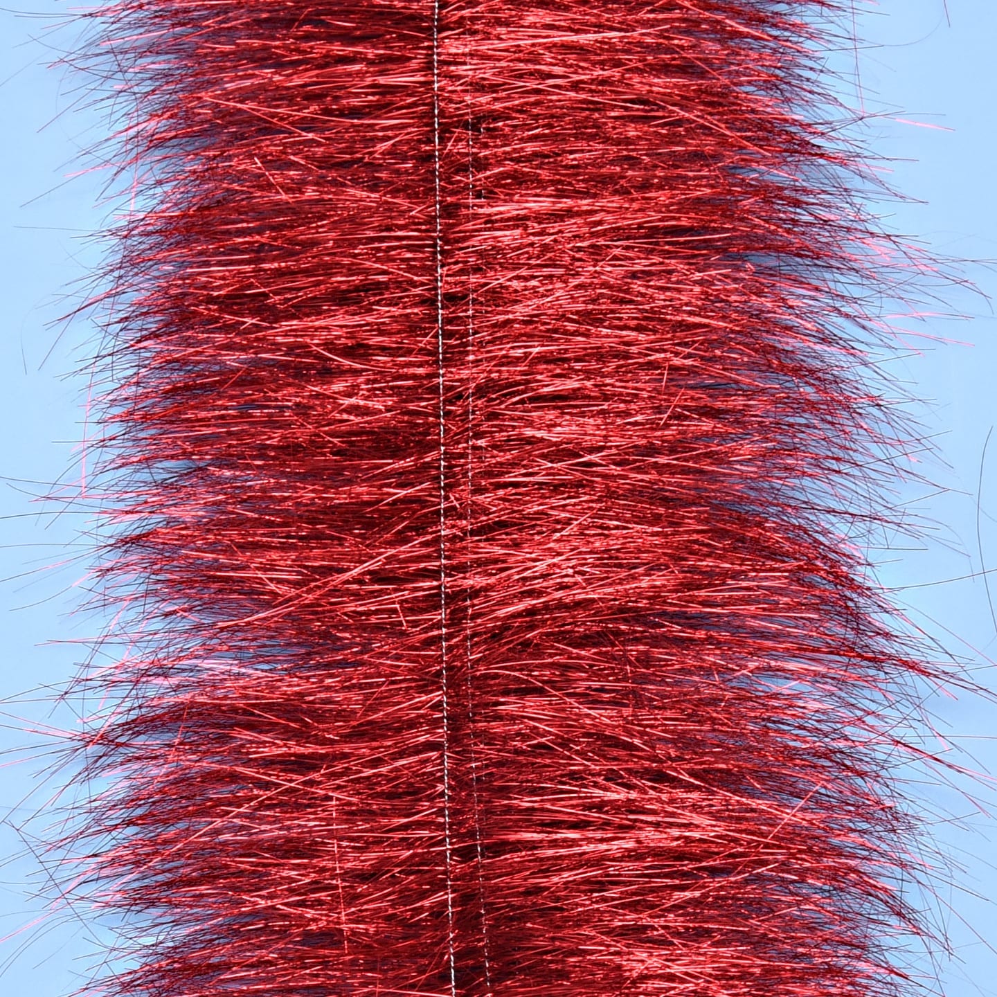 Red metallic sparkle brush with dense shimmering tinsel fibers on a central wire against pale blue background for fly tying