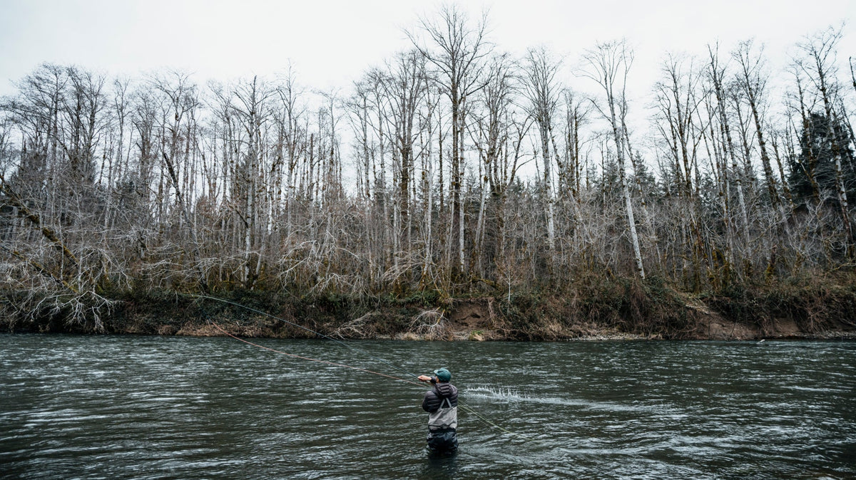 Wading angler casting a Redington Classic Spey fly reel setup in a river with leafless winter trees on the bank