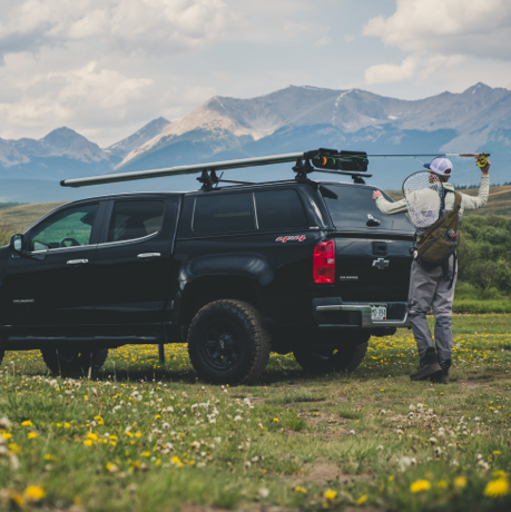 Black truck with Riversmith Euro River Quiver fishing rod rack mounted on roof, mountains in background