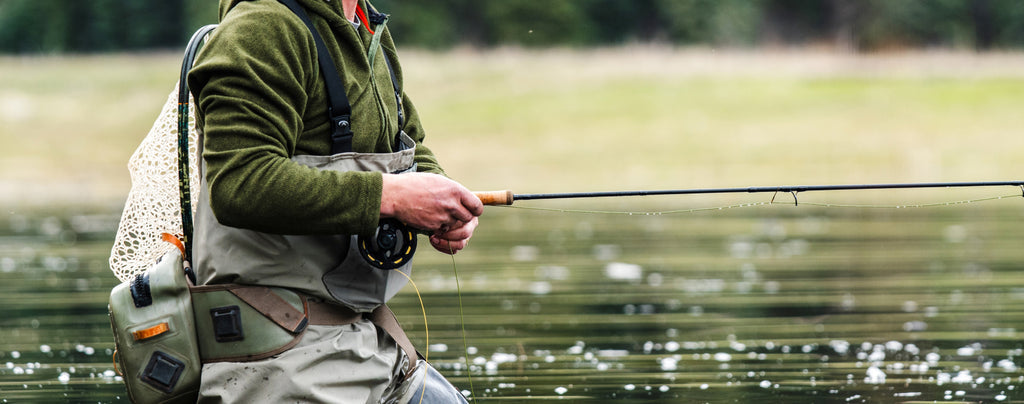 Angler in waders holding Redington EDC Tactical Edition fly rod while fishing in river with net attached