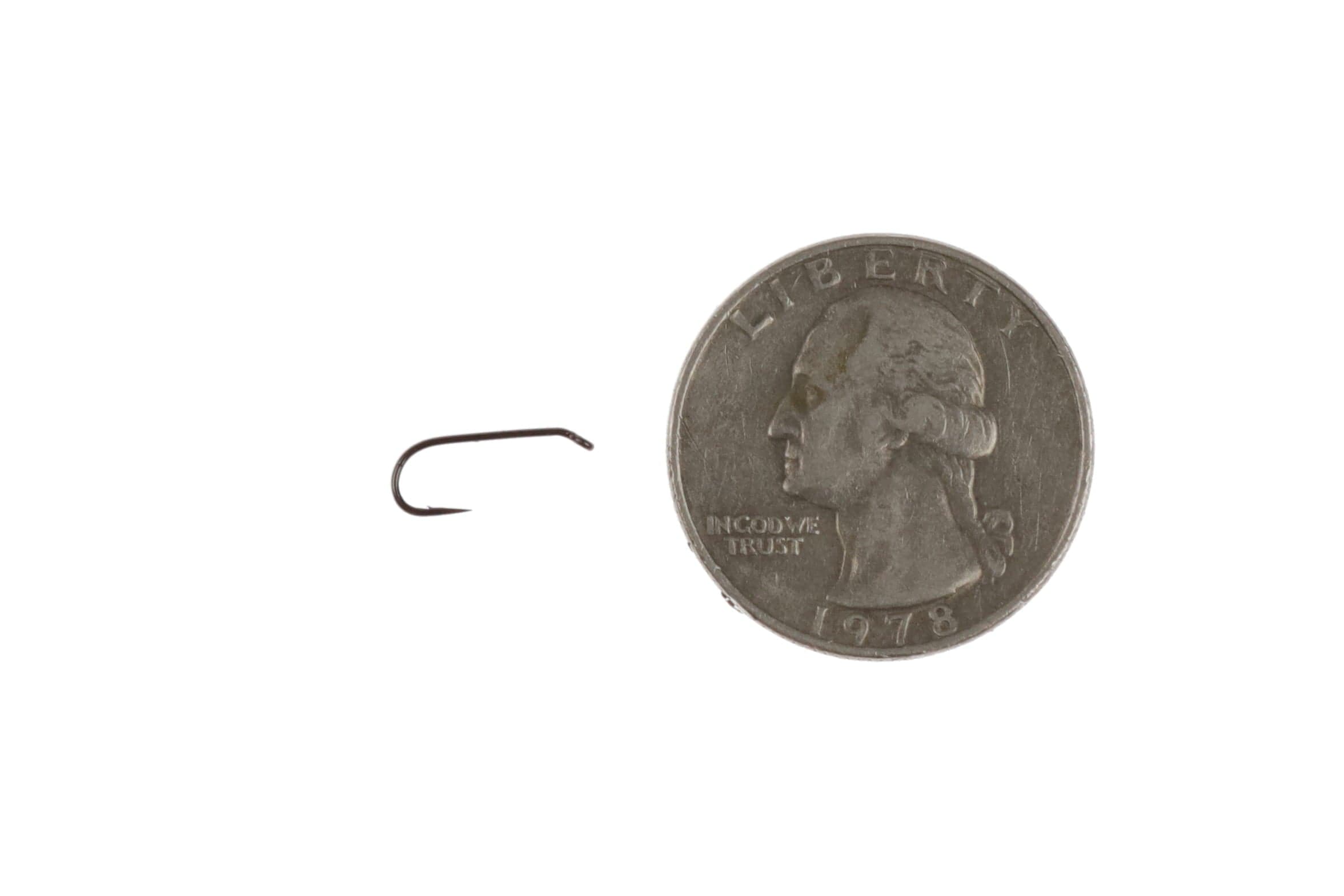 Dark bronze metal dry fly hook with short shank and upturned eye beside a quarter for scale, fly tying