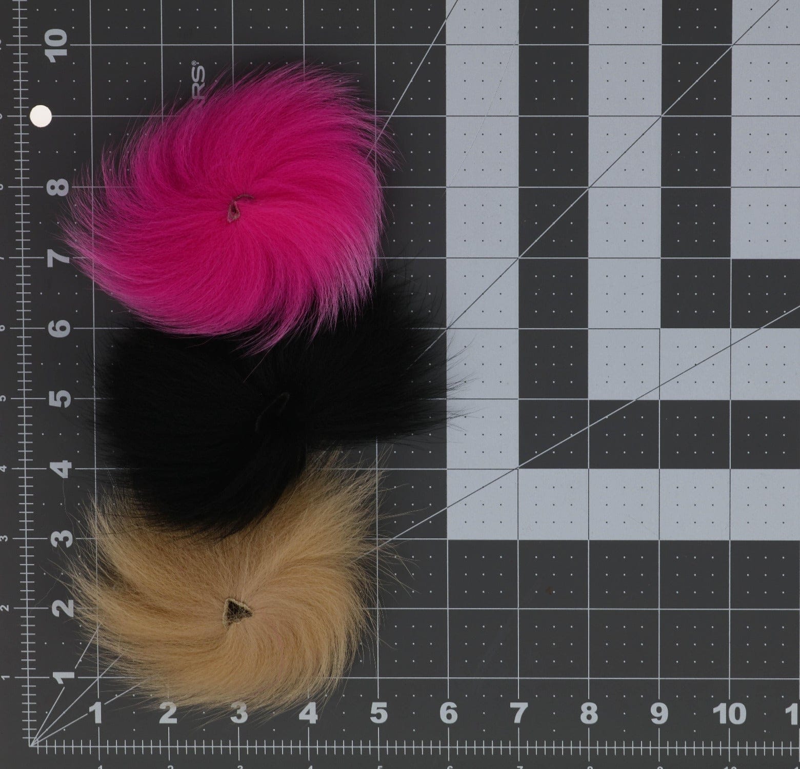 Three blue fox fur patches for fly tying: round fluffy hot pink, black, and tan body fur with stitched centers on cutting mat