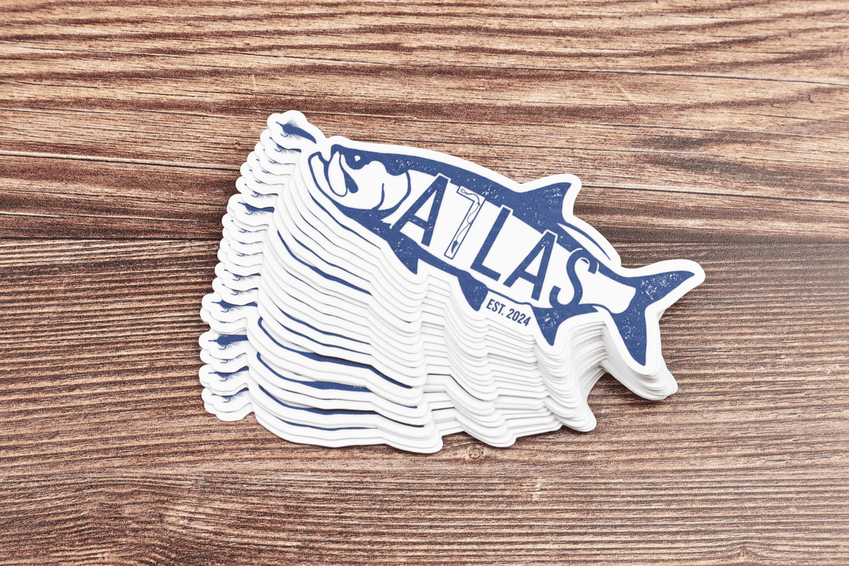 Stacked die-cut vinyl Atlas tarpon sticker in navy blue and white with distressed logo on wood grain background