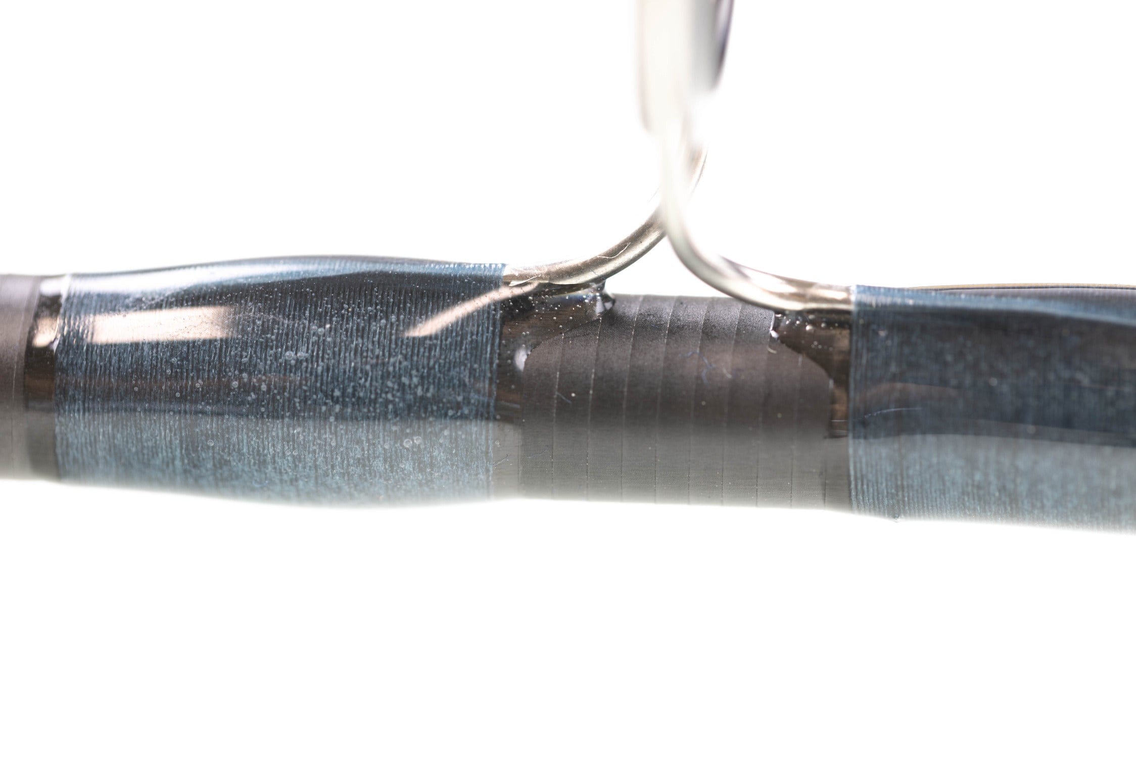 Close-up of Atlas fly rod mid-section showing glossy blue thread wraps, graphite blank, and silver guide foot under epoxy