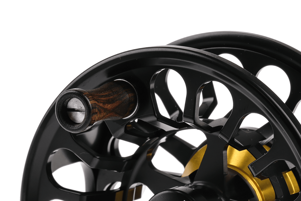 Bauer RX fly reel close-up, matte black anodized aluminum spool with wooden handle and gold inner hub, vented design