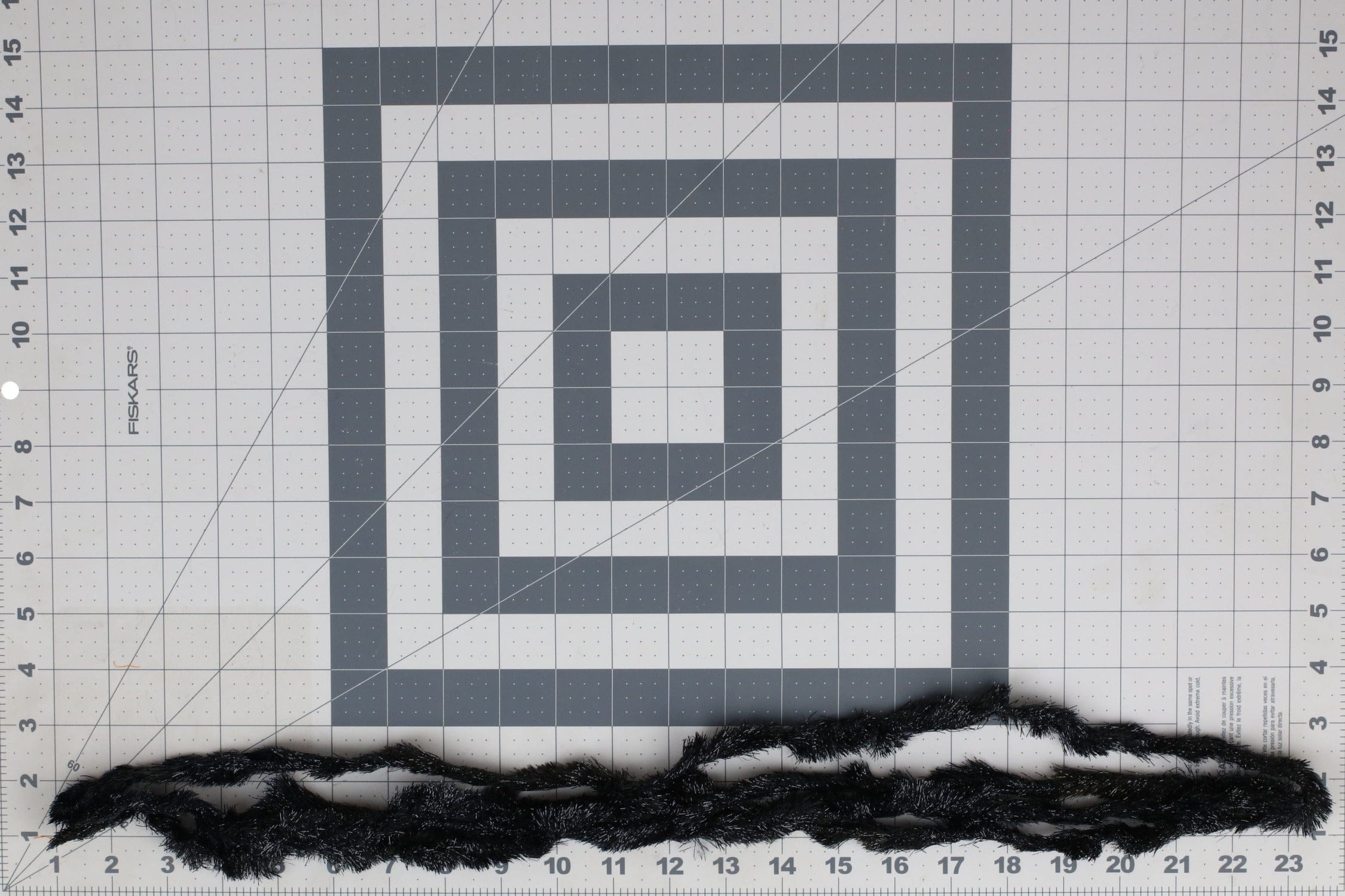 Black Gamechanger chenille strands with shiny tinsel fibers, fuzzy fly tying material on gridded cutting mat