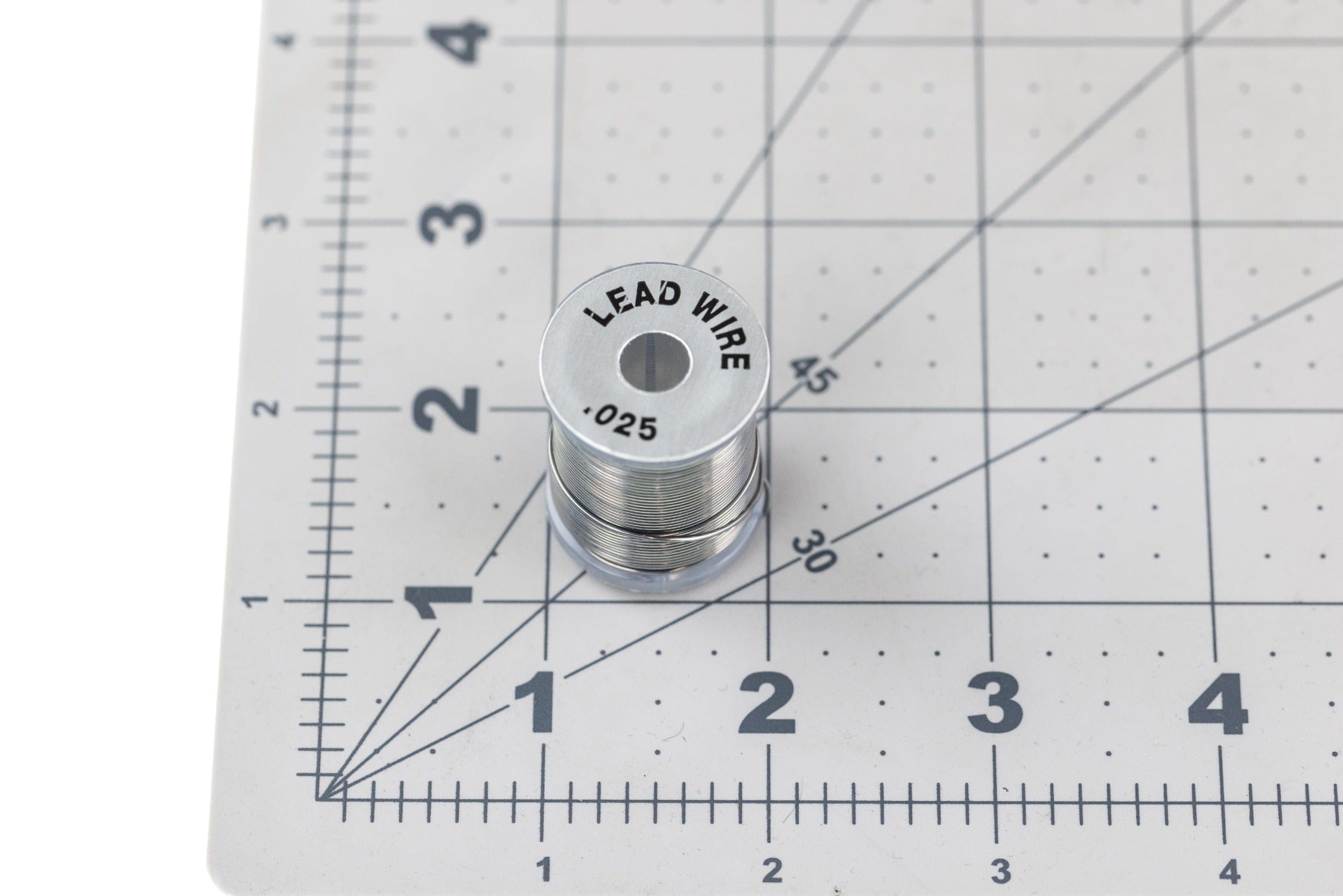 Silver Danville spooled lead wire (.025) stacked on gray ruler grid cutting mat for fly tying