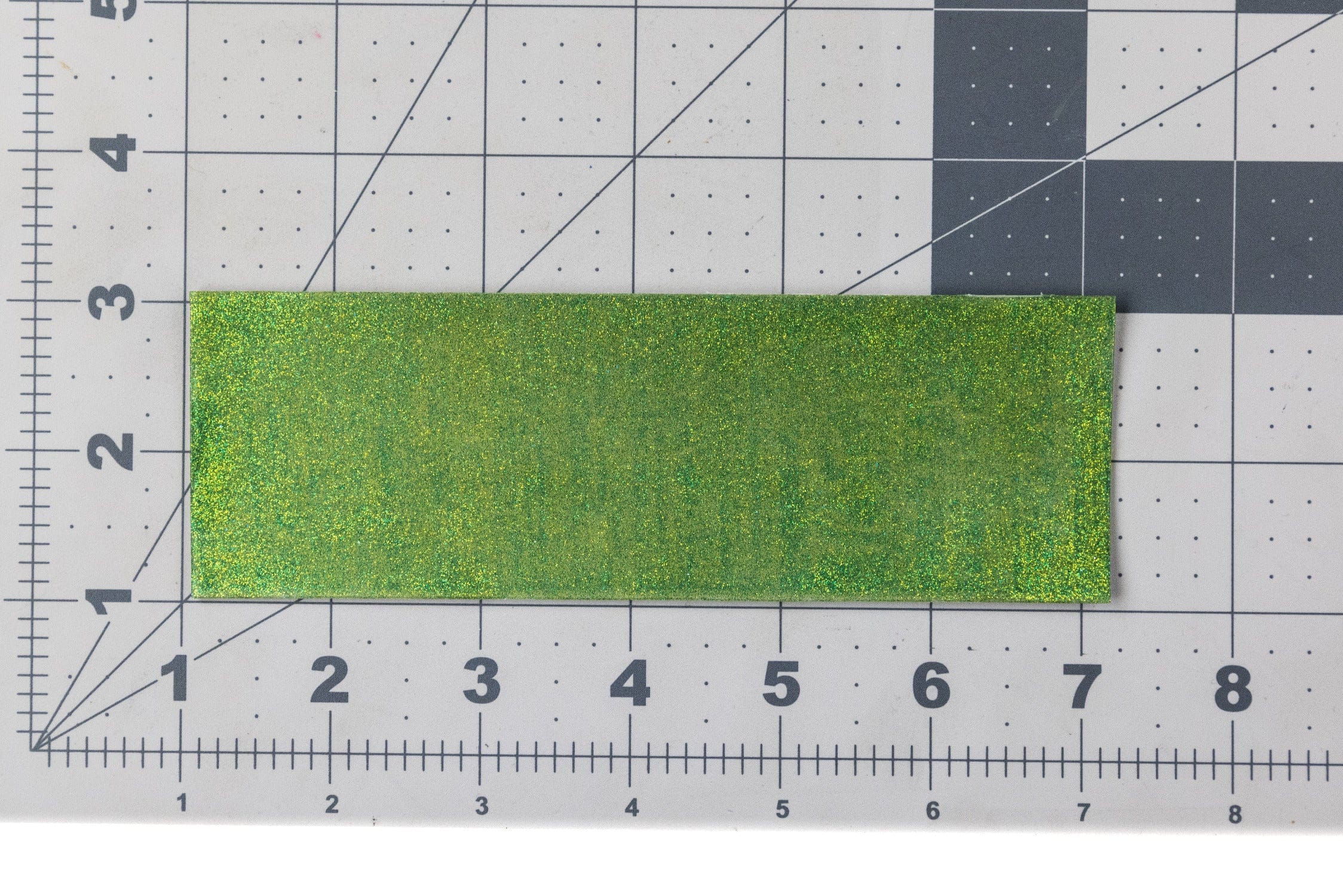 Green holographic Ds Flyes crystal skin sheet, rectangular glitter fly-tying material on gridded cutting mat
