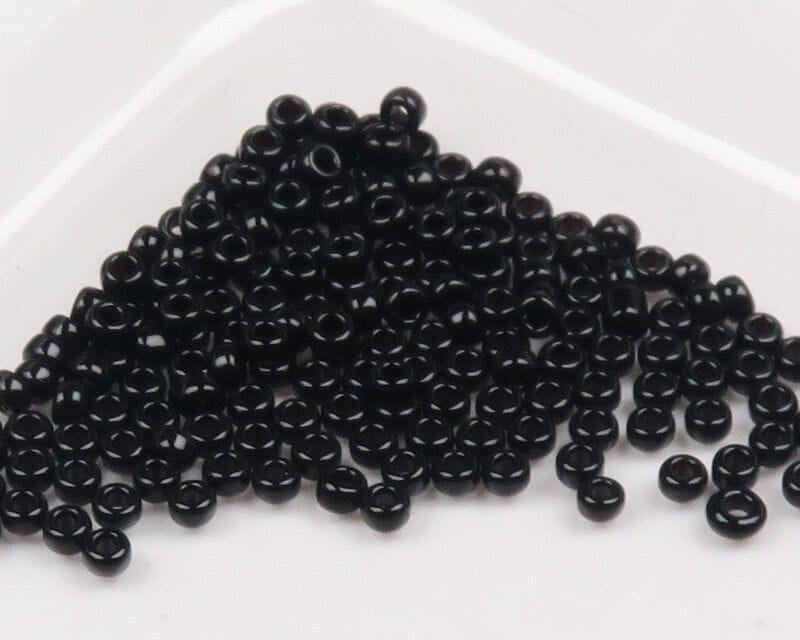 Glossy black glass beads with center holes, small round donut-style fly tying beads on white tray