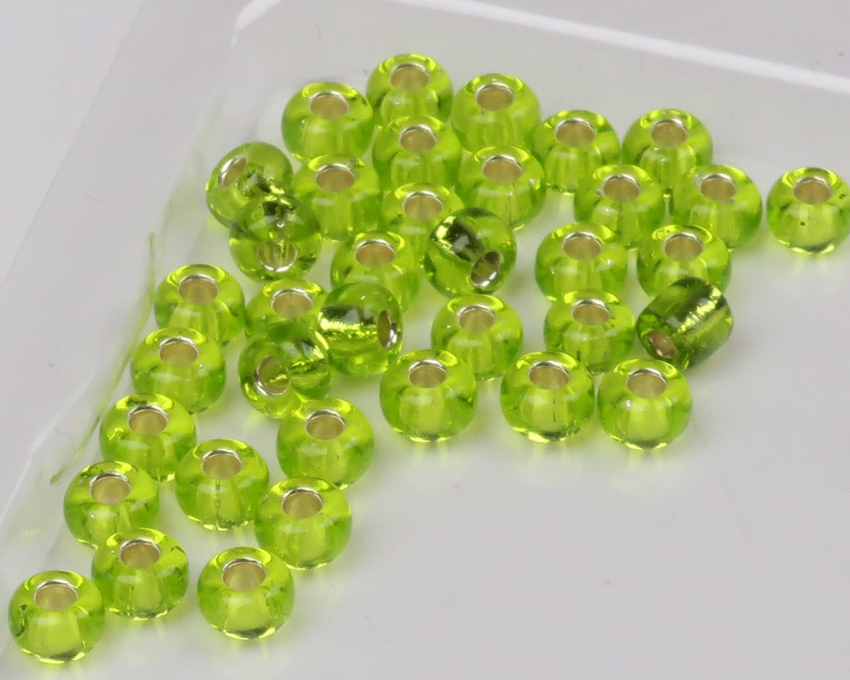 Translucent chartreuse glass fly tying beads with silver-lined holes, round seed-style beads on white background