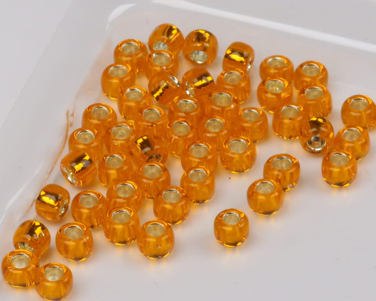 Amber orange translucent glass fly-tying beads with silver-lined cores on white tray