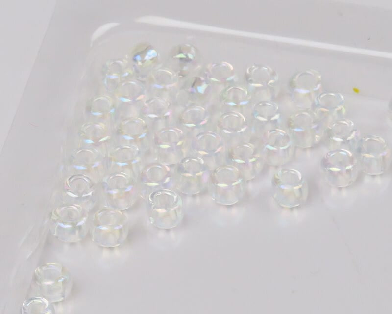 Clear iridescent glass beads for fly tying, small donut-shaped Ds Flyes beads scattered on white background