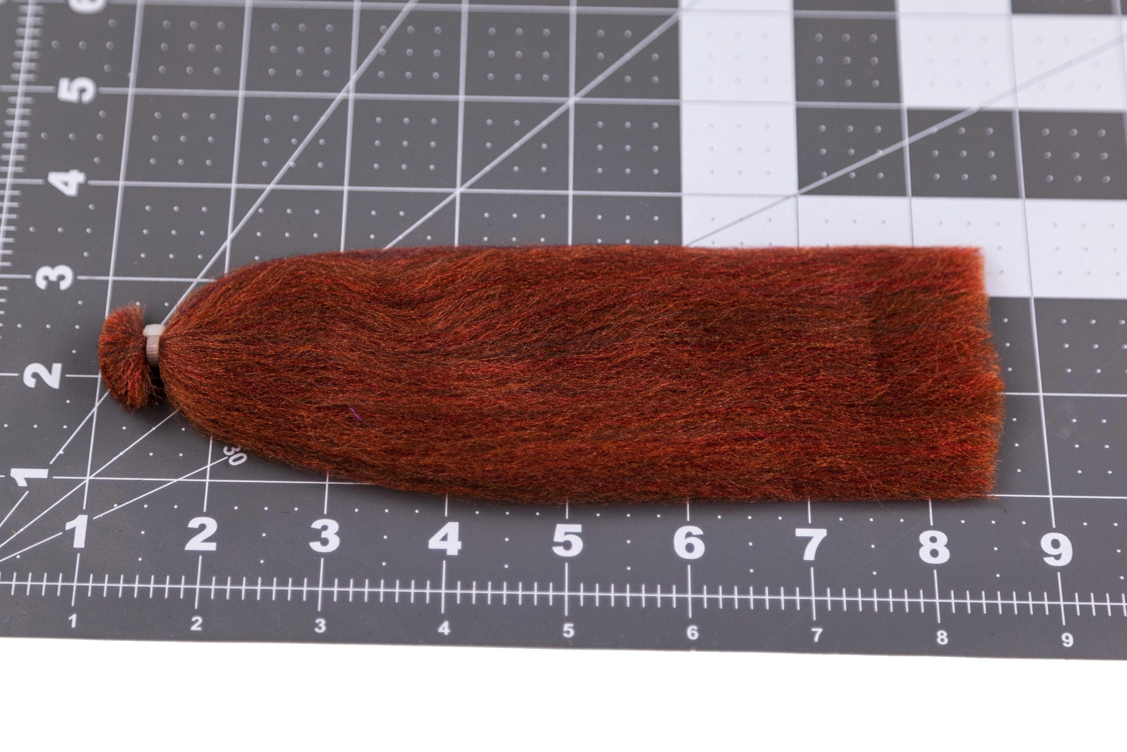 Rusty red-brown 3D silky fibers bundle tied at one end on grid cutting mat, fly tying material with subtle orange highlights