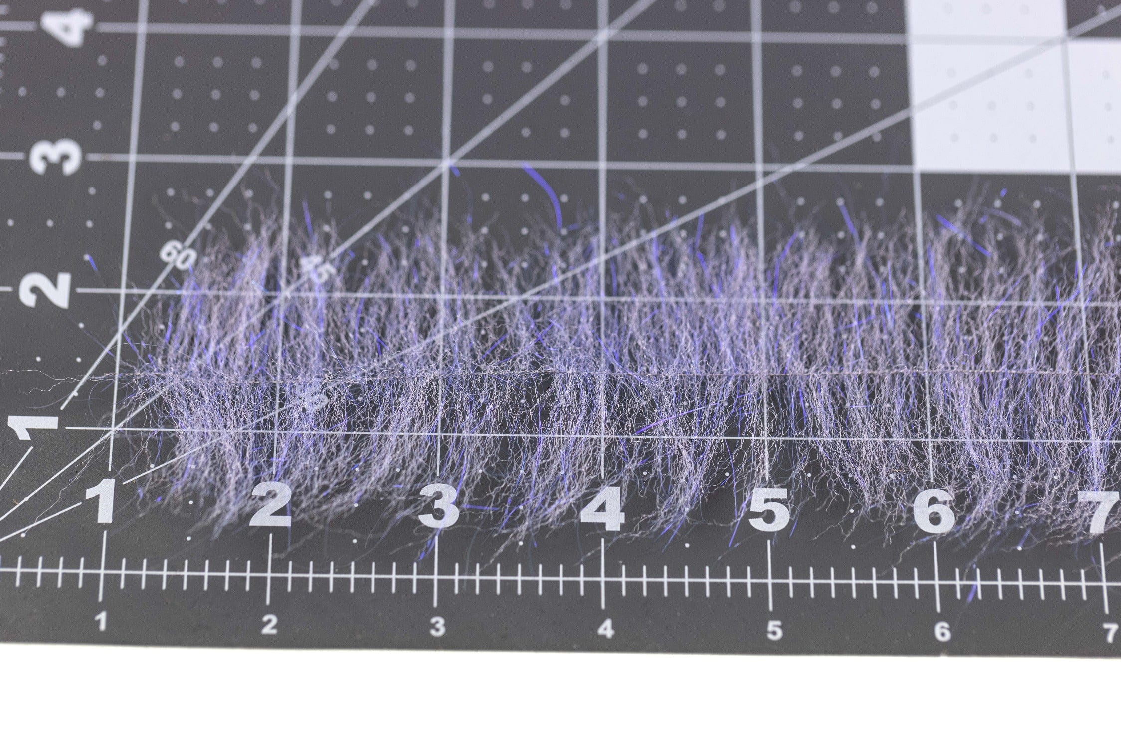 Lavender synthetic Anadromus brush fibers for fly tying, wispy hair-like strands on black measuring grid