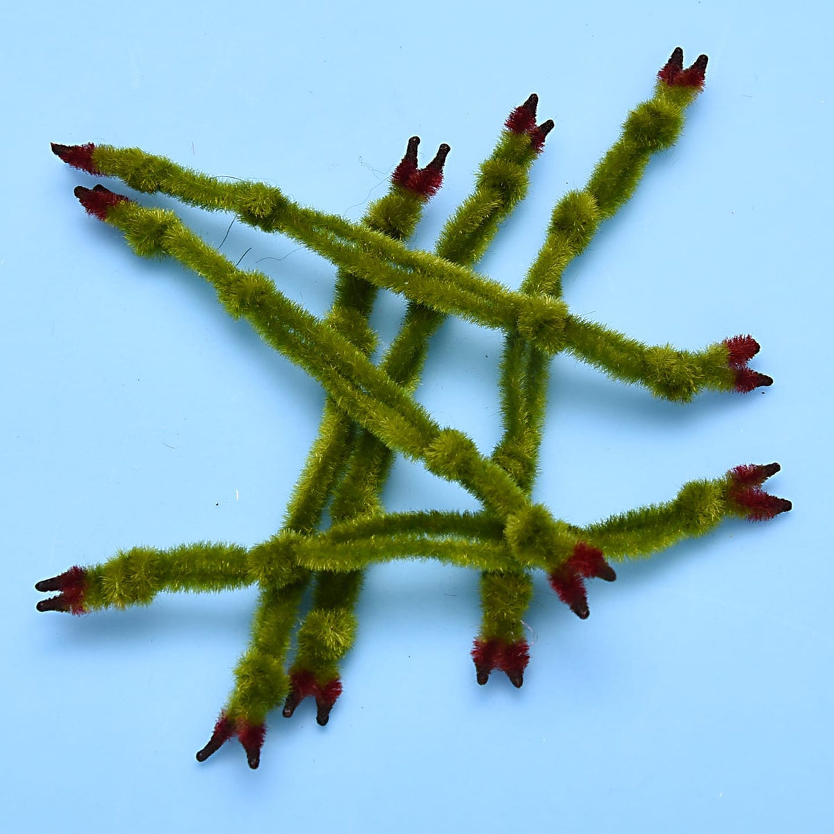 Olive-green fuzzy chenille crab claws with red-tipped split ends for fly tying, several laid on light blue background