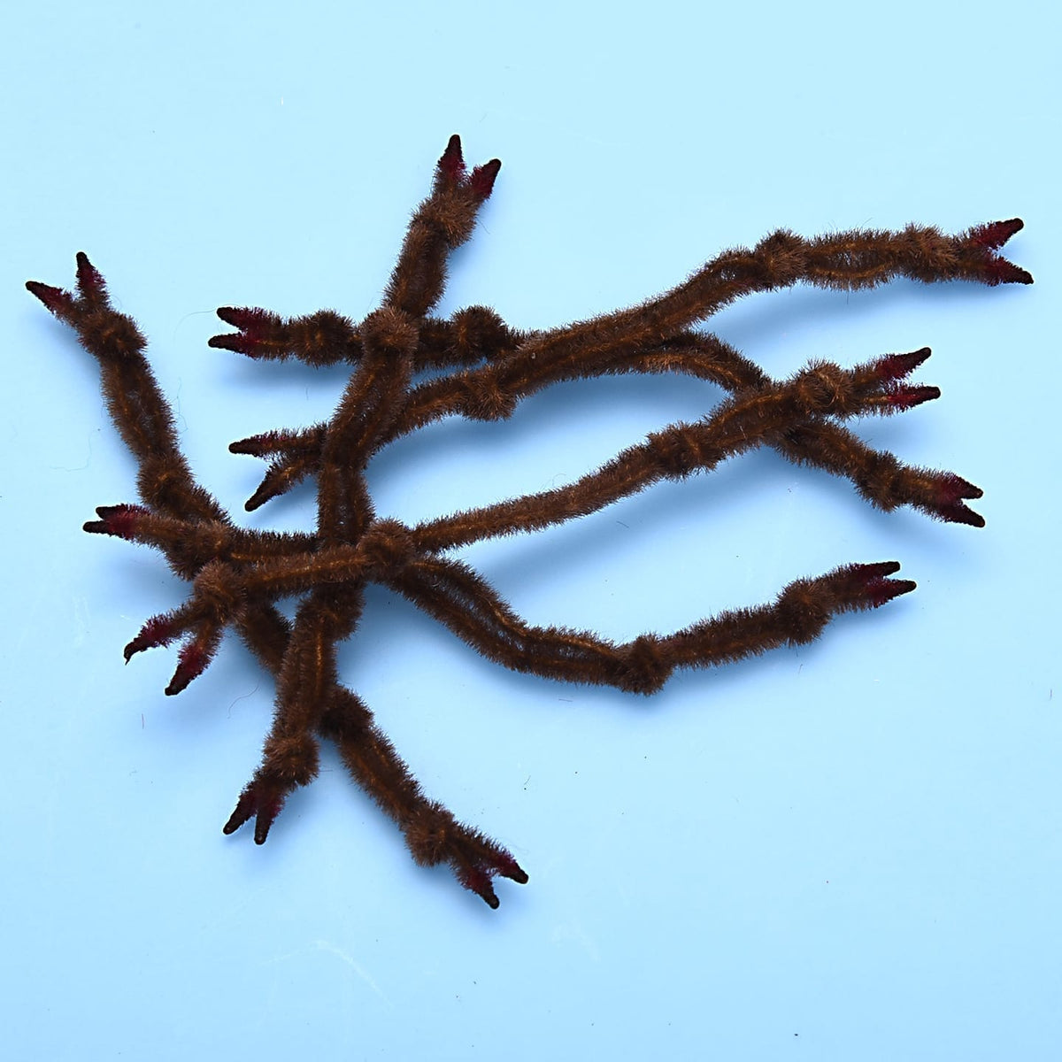 Brown fuzzy synthetic crab claws with red-tipped split ends for fly tying, multiple segmented stems on light blue background