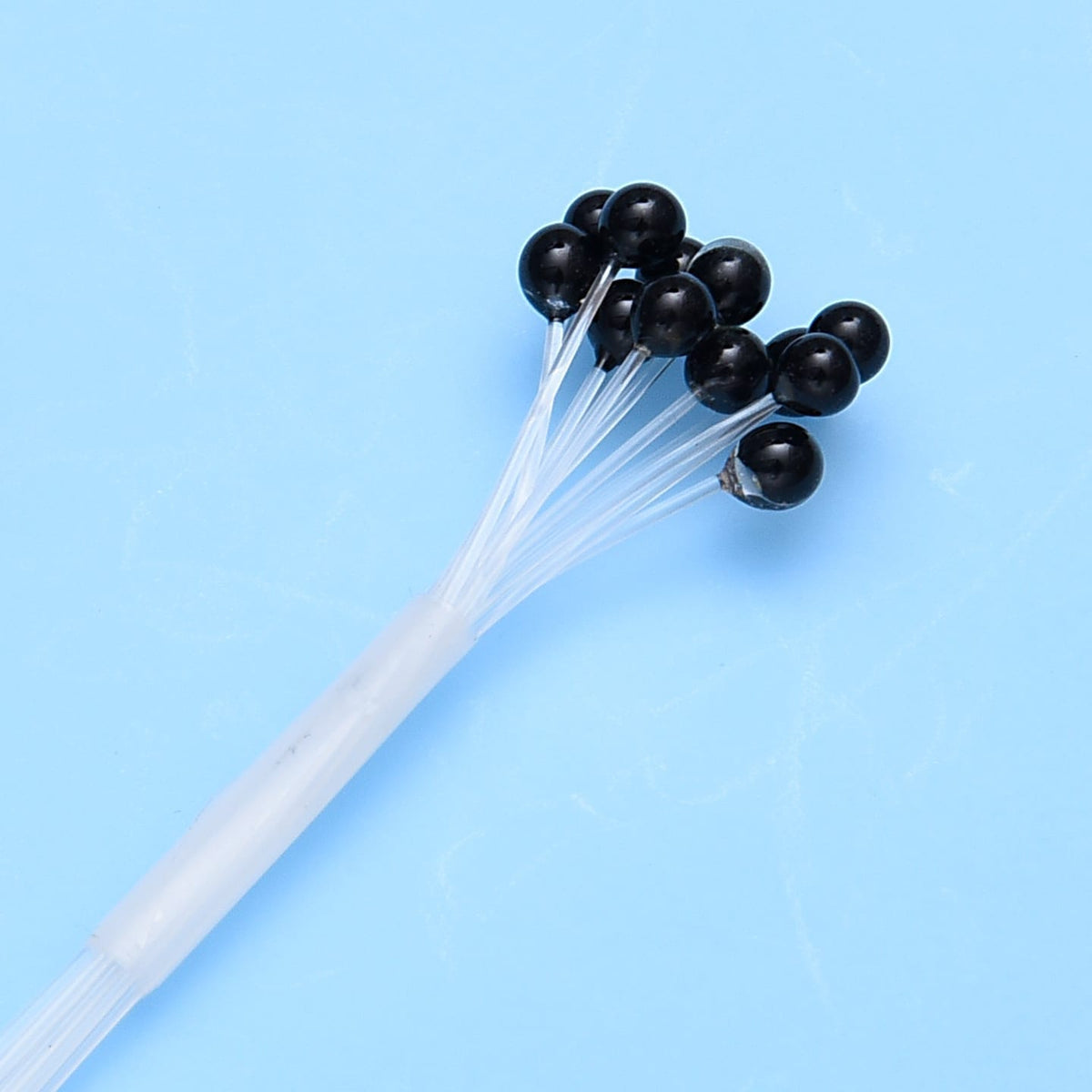 Black glossy crab and shrimp fly-tying eyes on clear silicone stems bundled on a translucent tube against blue background