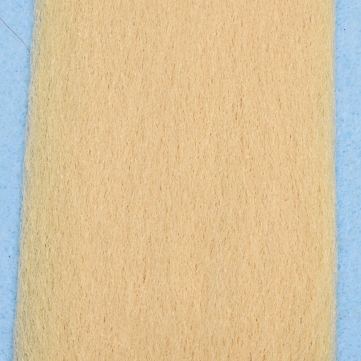 Pale tan synthetic EP Fibers sheet with fine, hair-like fibers on blue backing for fly tying material
