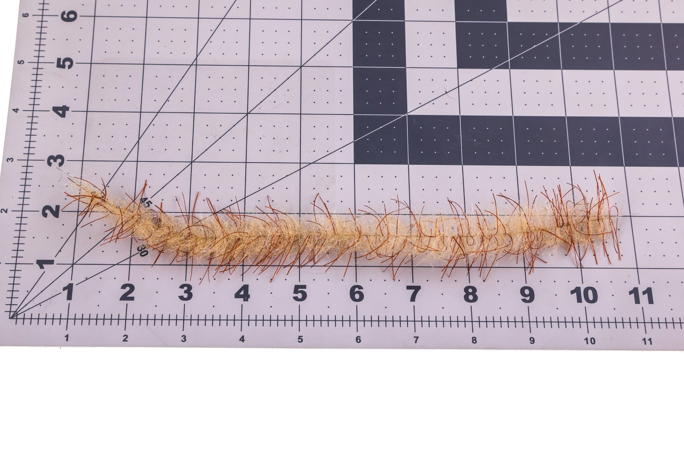 Tan Tarantula Hairy Legs fly tying brush strip with coppery stiff fibers on adhesive tape, laid on gridded cutting mat