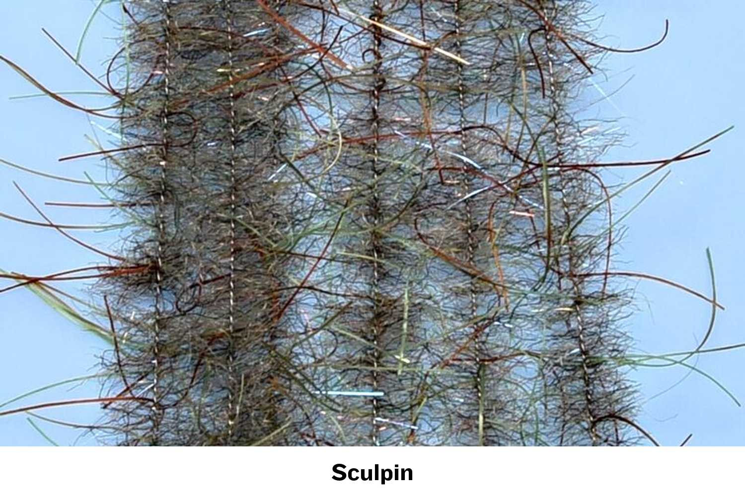 Olive-brown Woolly Critter brush strands with wispy orange and green synthetic hairs on a spined core for fly tying