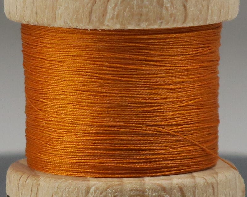 Bright orange pure silk thread wound on a natural wooden spool for fly tying, smooth lustrous texture