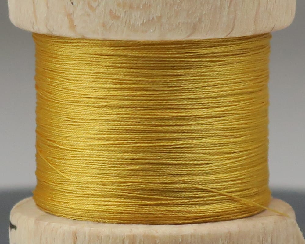 Golden yellow pure silk fly tying thread wound on a small wooden spool, smooth lustrous texture
