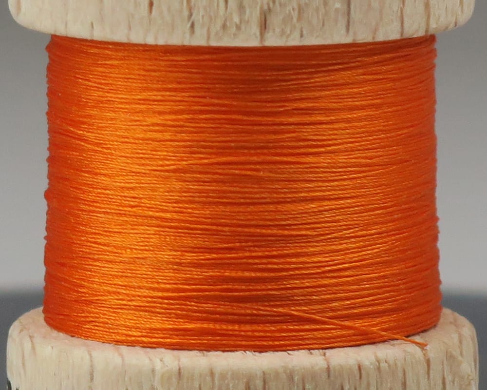 Bright orange pure silk thread wound on a small wooden spool for fly tying, fine glossy silk thread