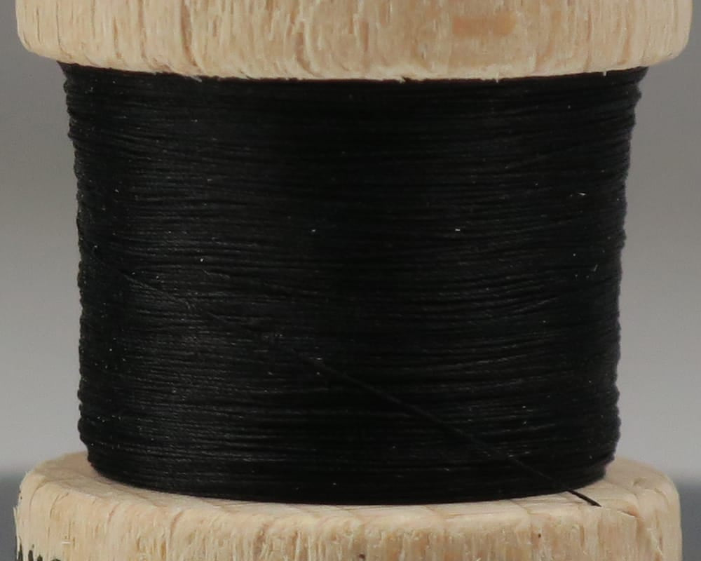 Ephemera pure silk thread in black tightly wound on small wooden spool, close-up for fly tying