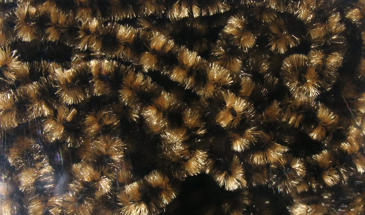 Black and golden-brown stonefly chenille with dense, sparkly fuzzy tufts and segmented texture for fly tying