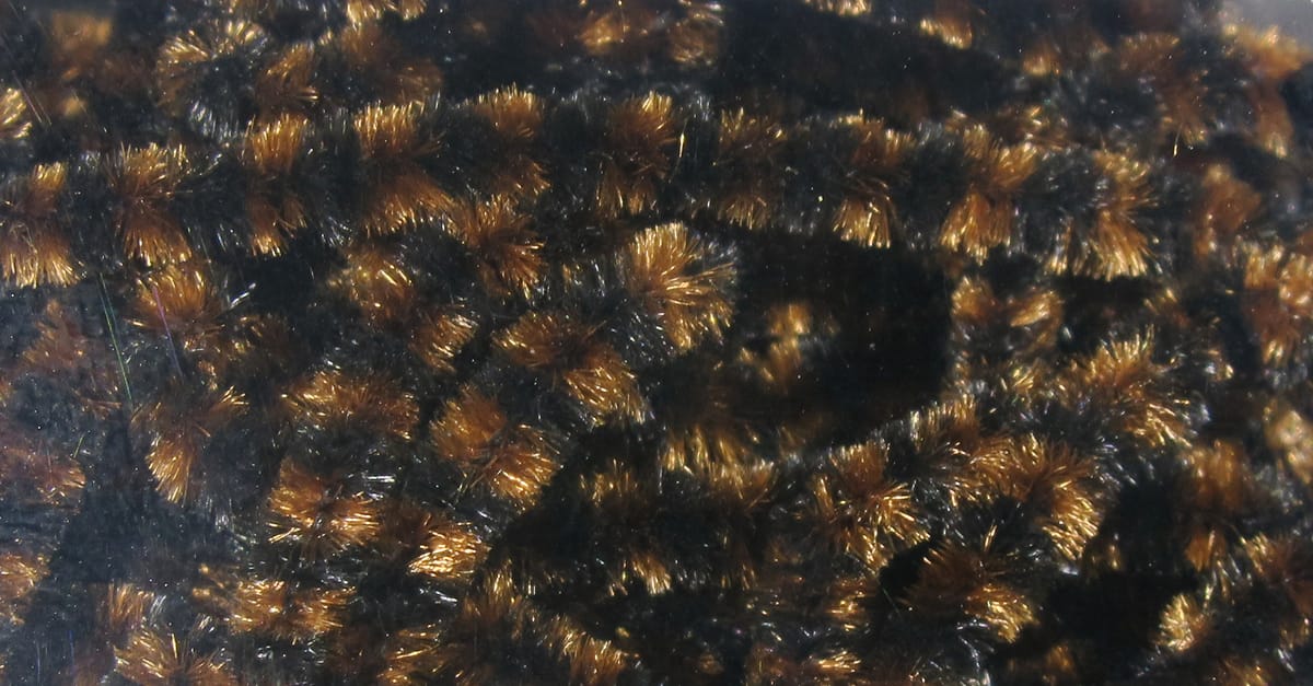 Black and copper stonefly chenille close-up showing dense fuzzy synthetic fibers with metallic highlights for fly tying