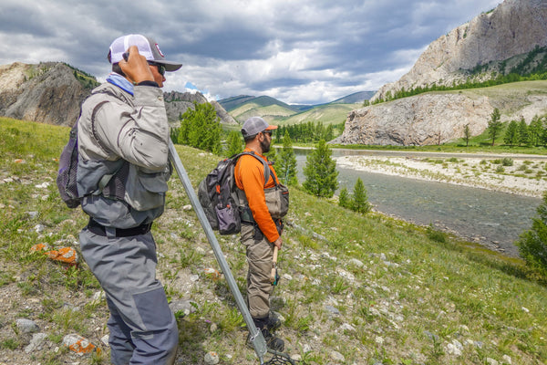 Two hikers with backpacks explore a scenic mountain river valley landscape during an outdoor expedition adventure