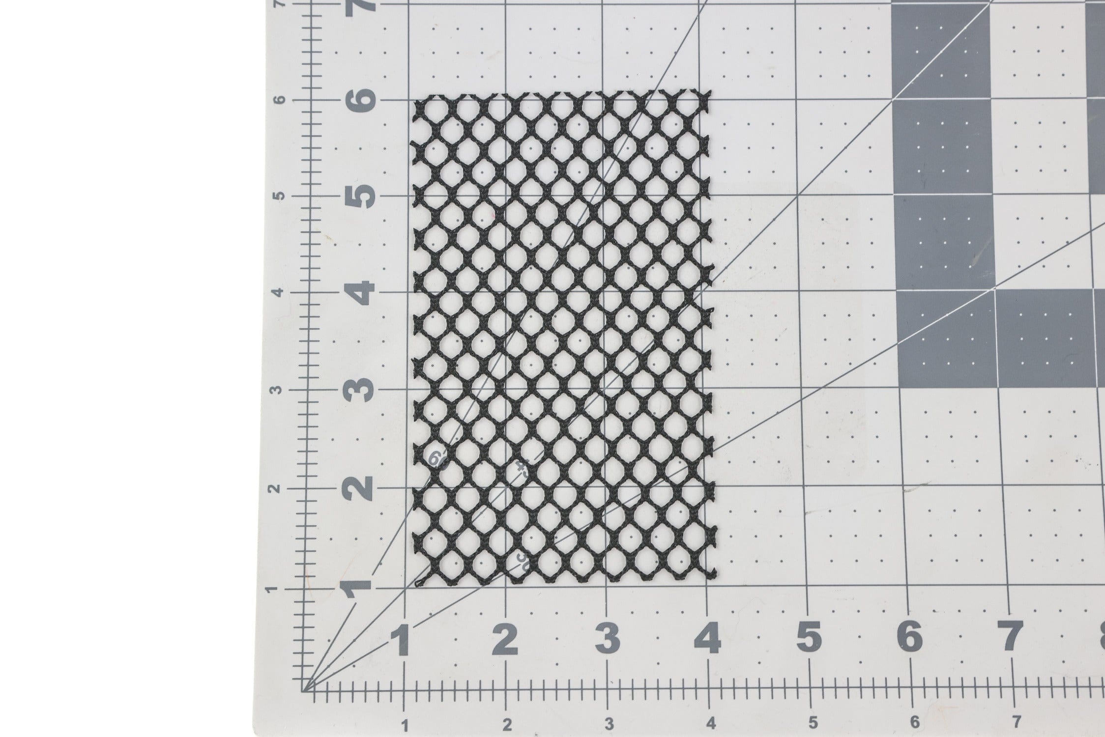 Hareline black honeycomb mesh patch, rectangular nylon pattern over gray cutting mat with ruler