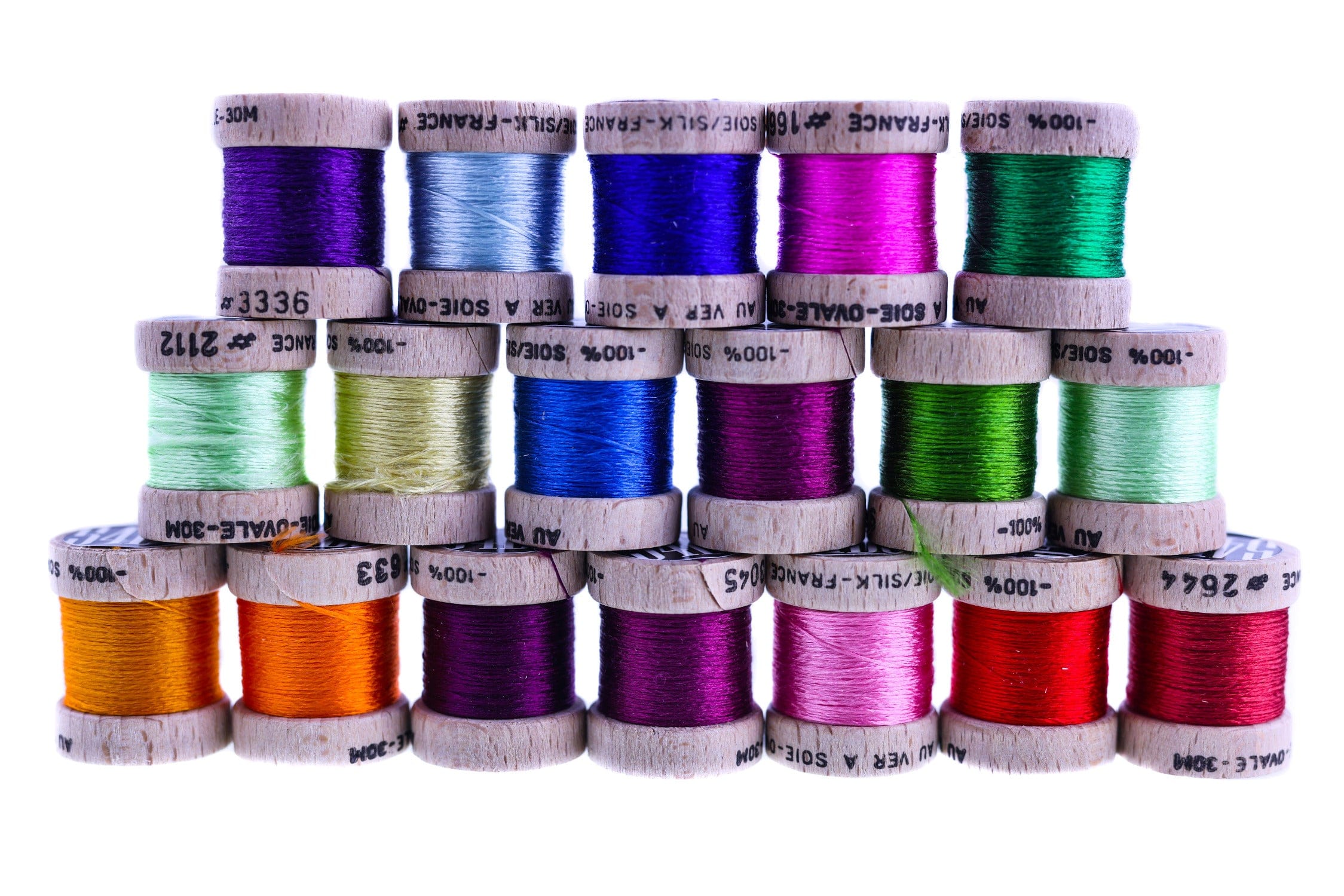 Stacked wooden spools of Hareline 54 Dean St. Ovale pure silk floss in bright jewel-tone colors for fly tying