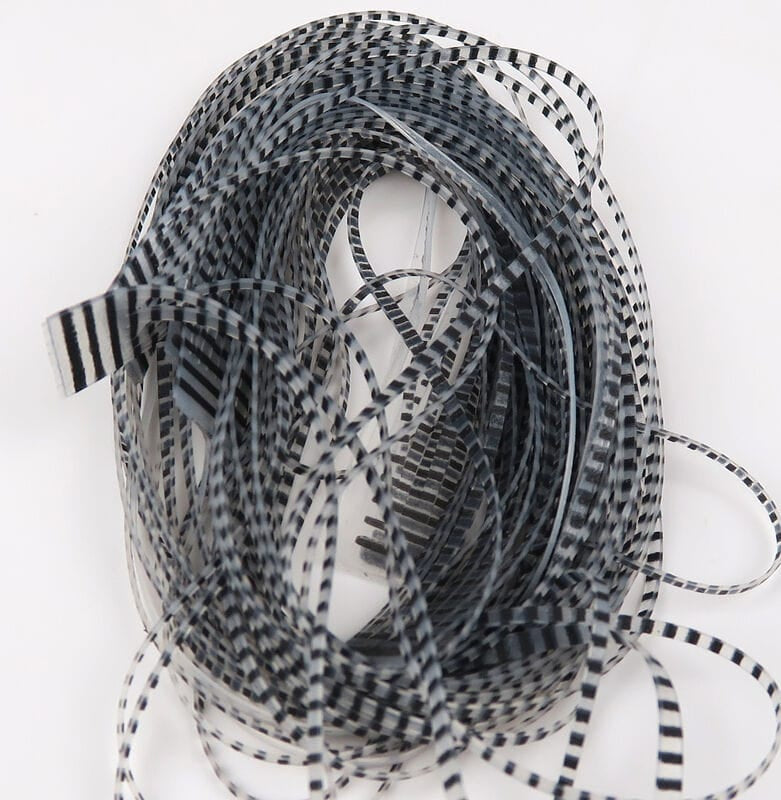 Coiled bundle of black-and-white barred synthetic crusher legs for fly tying, thin translucent strips with zebra-like bars