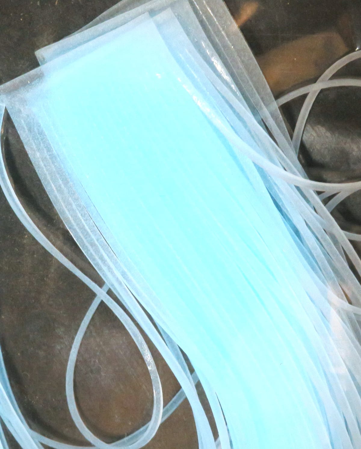 Translucent light blue Chicone's Crusher Legs, thin flexible silicone strips with barred texture for fly tying